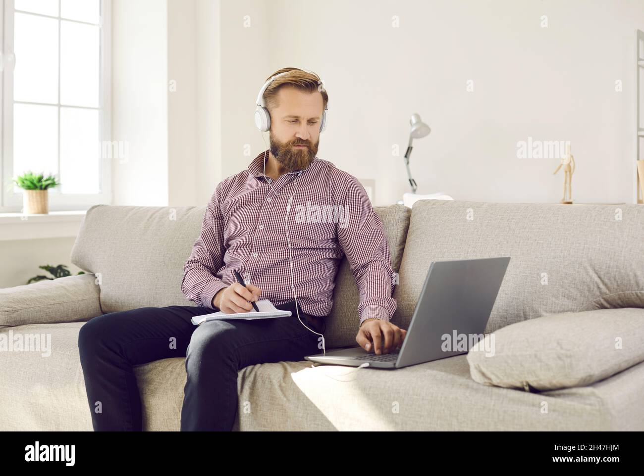L'homme adulte dans un casque d'écoute écouter de l'audio et de prendre des notes a une leçon d'e-learning en ligne. Banque D'Images