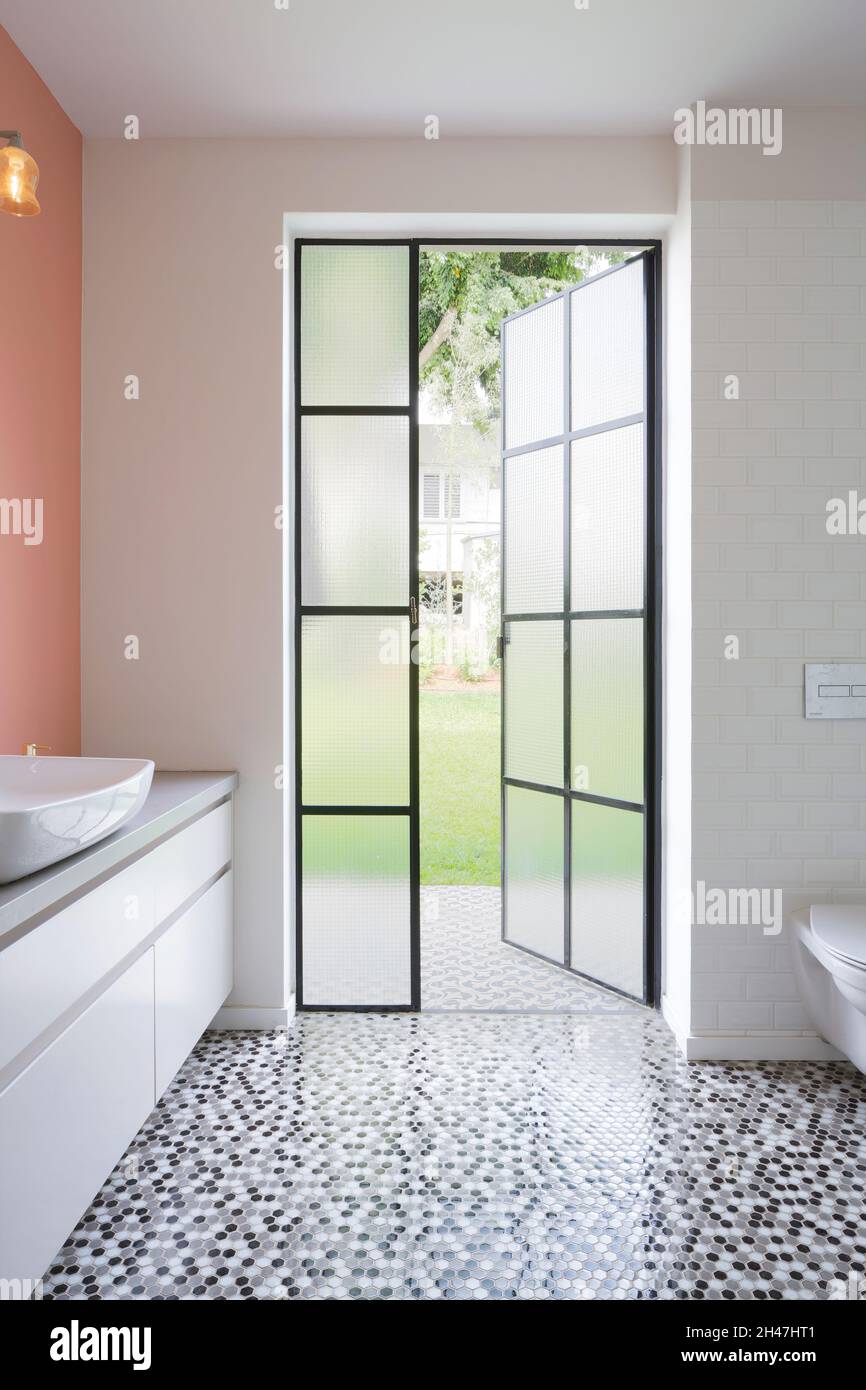 Salle de bains avec porte belge donnant sur le jardin.Un placard allongé avec un évier, un mur de couleur pêche et un luminaire suspendu au mur. Banque D'Images