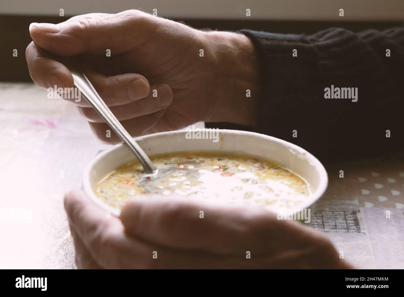 Un homme âgé mange de la soupe de nouilles en tenant une cuillère dans une main et en tenant une boîte de bouillon avec l'autre gros plan Banque D'Images