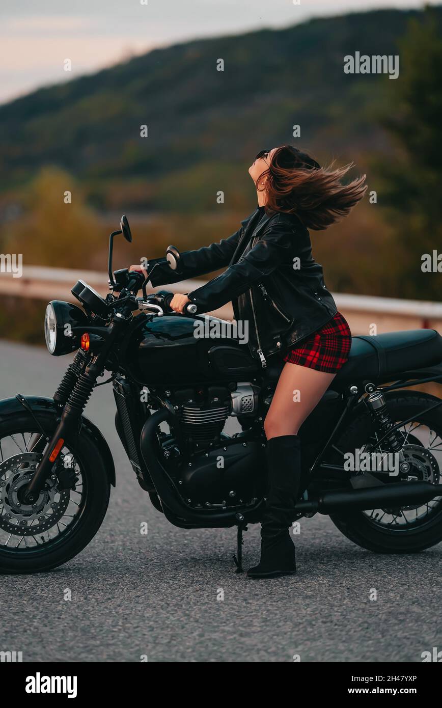 Portrait d'une femme moto assurée en mini jupe, veste en cuir sur une moto  de style rétro.Un conducteur attrayant dans des bottes de protection sur  route Photo Stock - Alamy