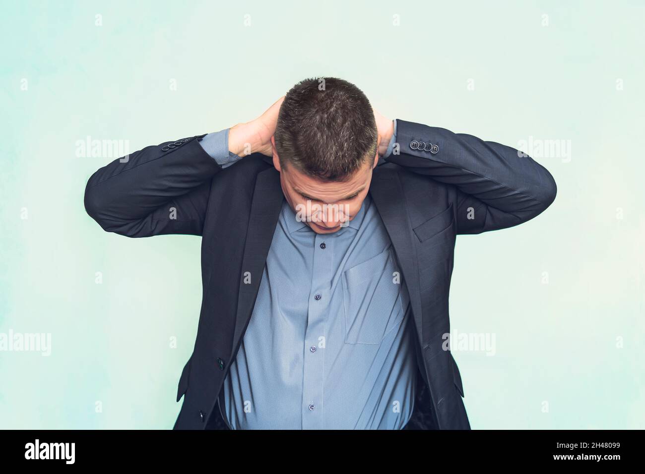 Homme d'affaires avec une raideur de la nuque ou de la tension mal de tête tenant ses mains derrière sa tête tout en grimaquant dans la douleur sur un fond bleu. Concept médical Banque D'Images