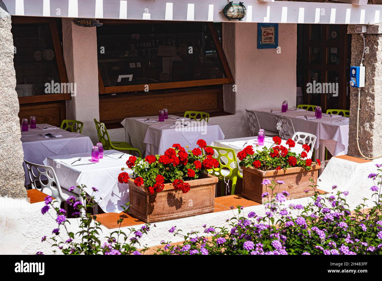 Tables de repas de restaurant à l'ombre d'une marquise en bois avec vue sur la rue et la mer dans la zone commerçante du bijou en bord de mer à Baia Sardaigne. Banque D'Images