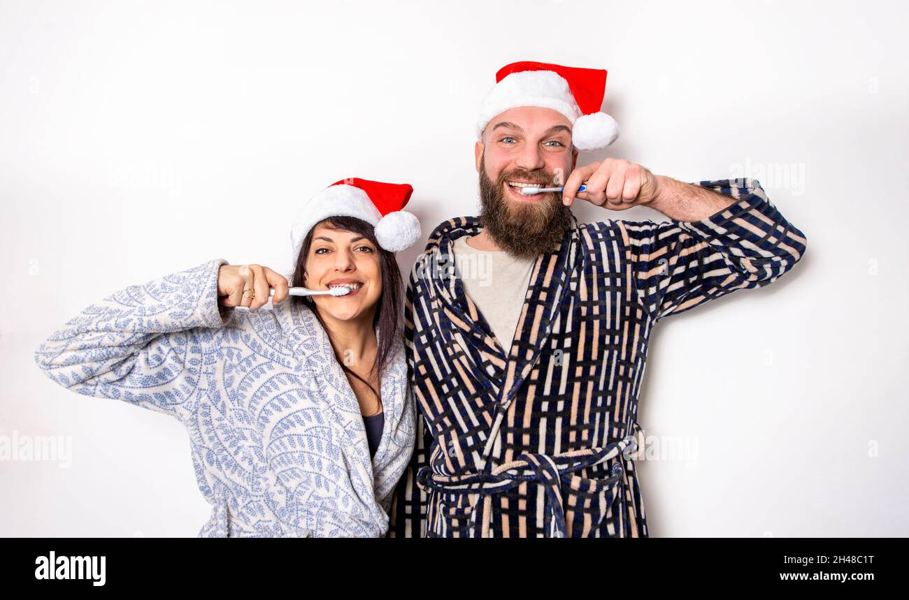 joyeux noël !Jeune couple adulte célébrant Noël temps portant chapeau de père noël debout isolé contre fond mur se brossant les dents. Famille Banque D'Images