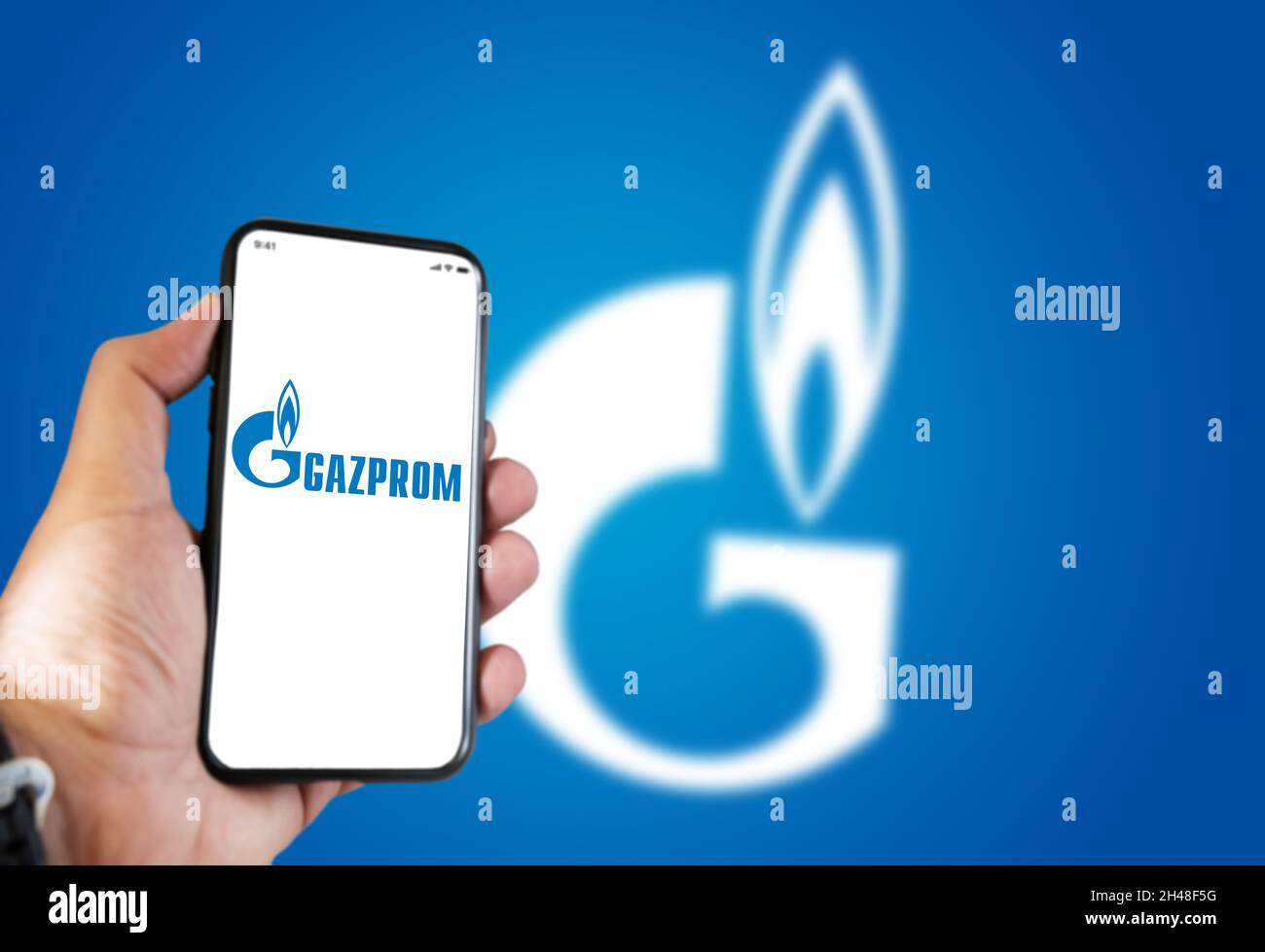 Saint-Pétersbourg , RUS, octobre 2021 : main tenant un téléphone avec l'application mobile Gazprom à l'écran et le logo flou sur fond bleu.Gazpro Banque D'Images