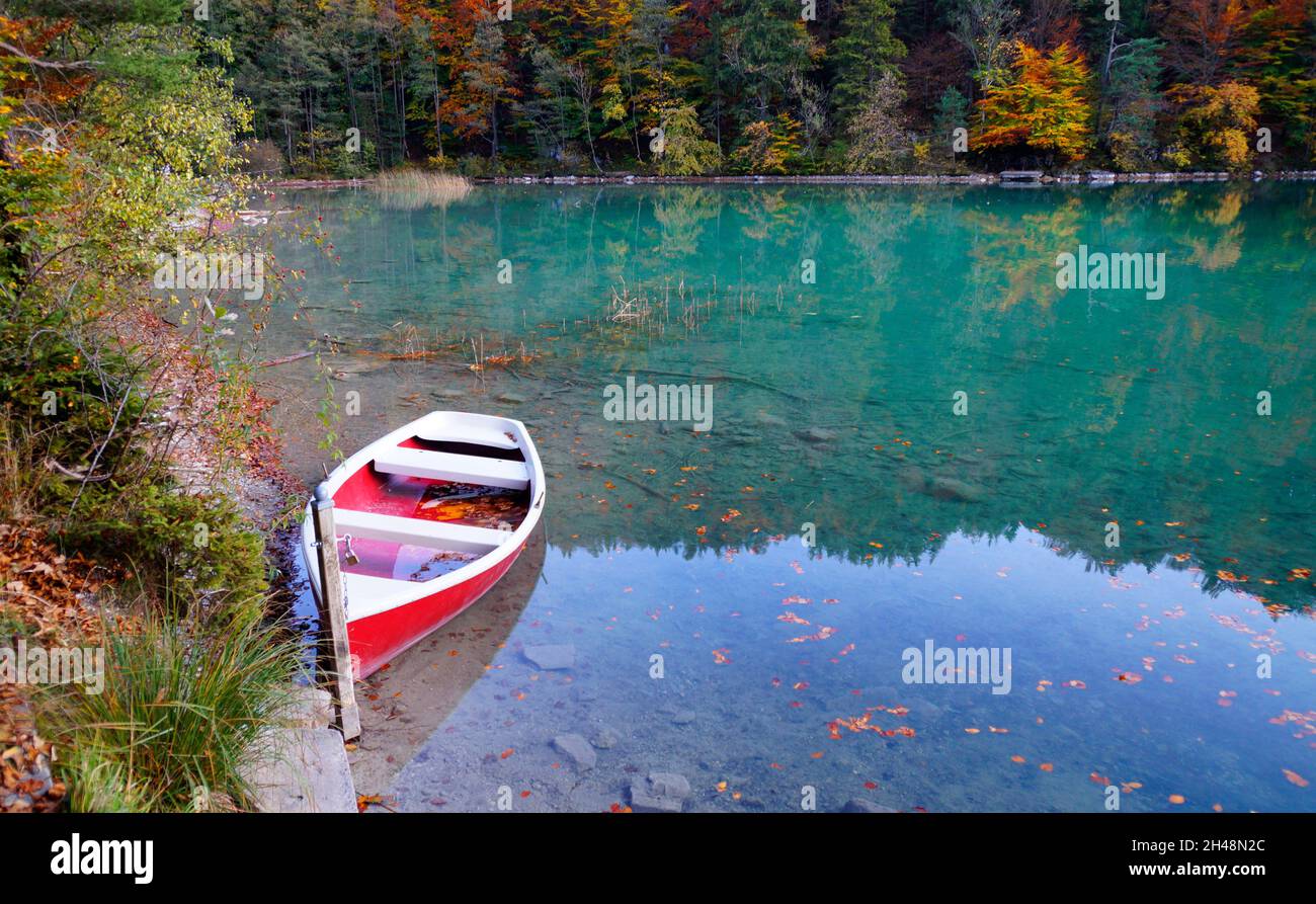 Une vue panoramique sur le lac Alatsee et un bateau rouge reposant sur l'eau vert émeraude lors d'une belle journée d'automne (Bavière en Allemagne) Banque D'Images