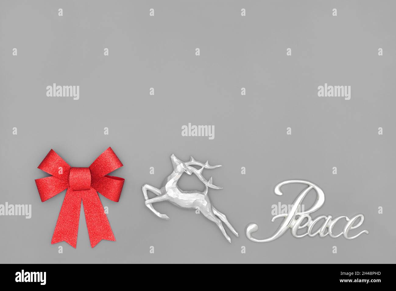 Concept de paix à Noël avec signe argenté, renne, noeud rouge scintillant sur fond gris.Composition abstraite pour les fêtes. Banque D'Images