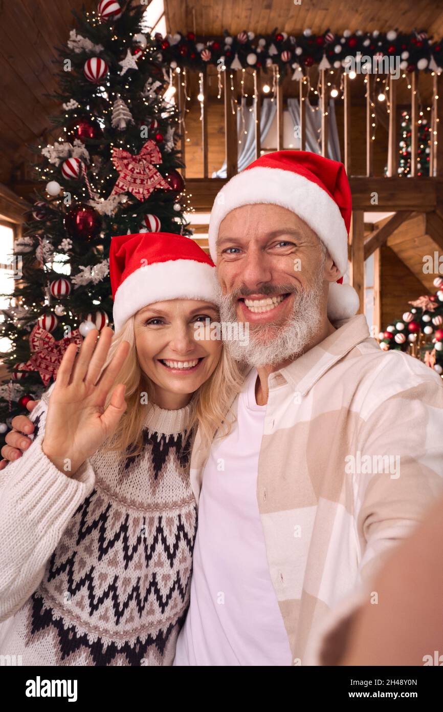 Joyeux couple d'âge mûr saluant la famille lors d'un appel vidéo de Noël, vue caméra mobile. Banque D'Images