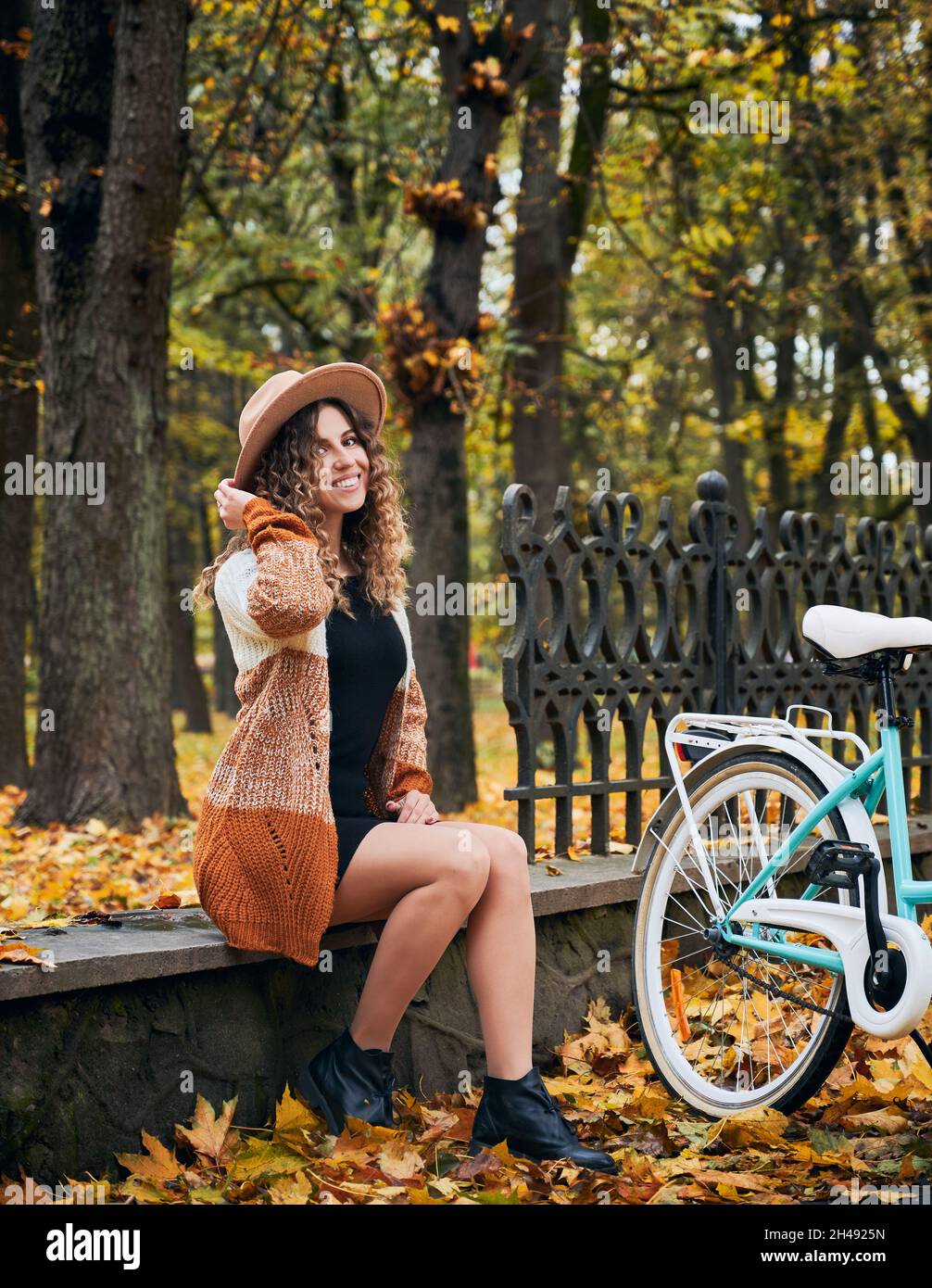 Portrait d'une mignonne de motard curly qui se repose dans un parc d'automne avec un cycle de ville rétro.Marche à l'extérieur à vélo.De belles activités de loisirs en vélo par temps frais d'automne. Banque D'Images