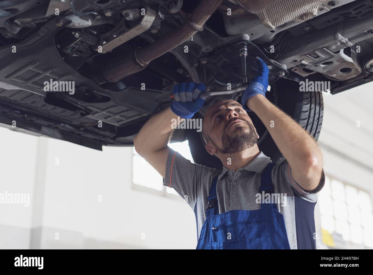 Mécanicien professionnel travaillant sous une voiture, il effectue une inspection du véhicule et vérifie l'absence de fuites Banque D'Images