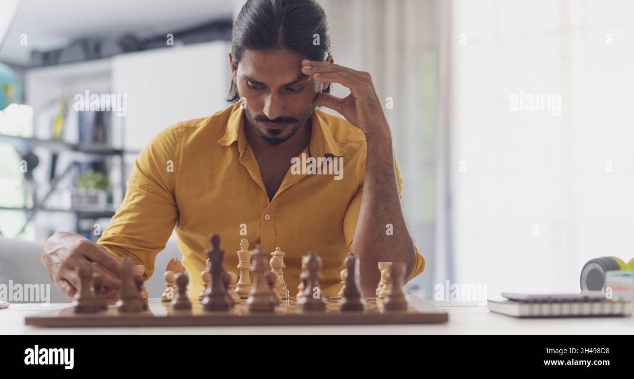 Homme intelligent jouant aux échecs à la maison, il est en mouvement des pièces sur l'échiquier et la pensée, le concept de jeux de stratégie Banque D'Images