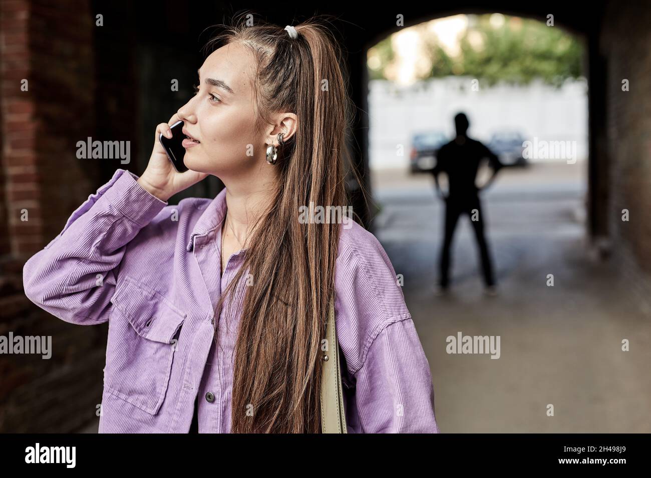 Portrait de la jeune femme caucasienne parlant au téléphone ne soupçonnait même pas qu'elle est suivie par Criminal Bandit dans l'arrière-plan debout A Banque D'Images