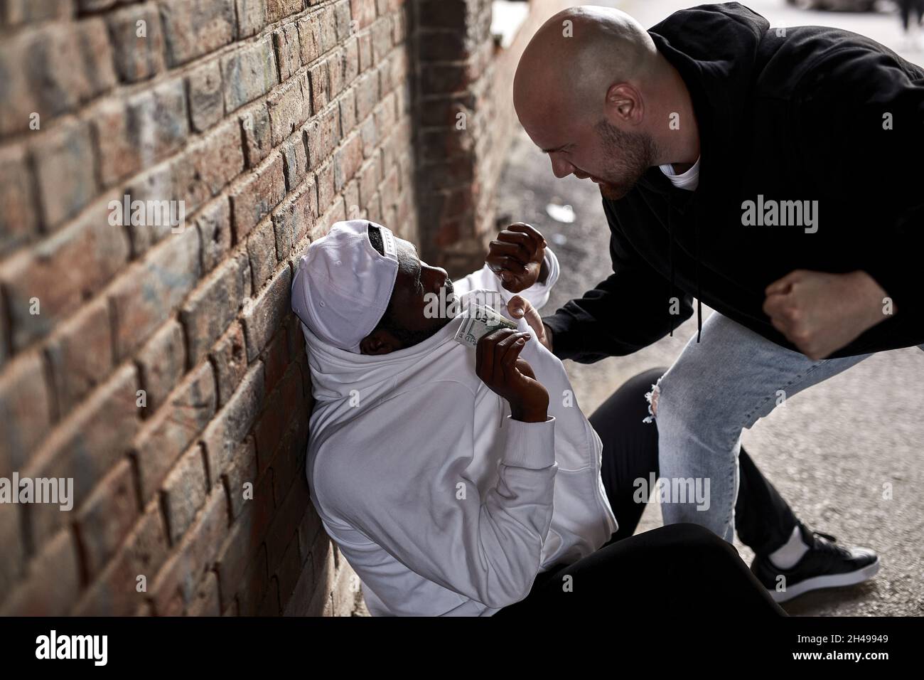 Vue de côté sur le dangereux Bandit Hooligan caucasien exigeant de l'argent de jeune Africain américain étranger, menaçant, effrayé Homme donne de l'argent à Thi Banque D'Images