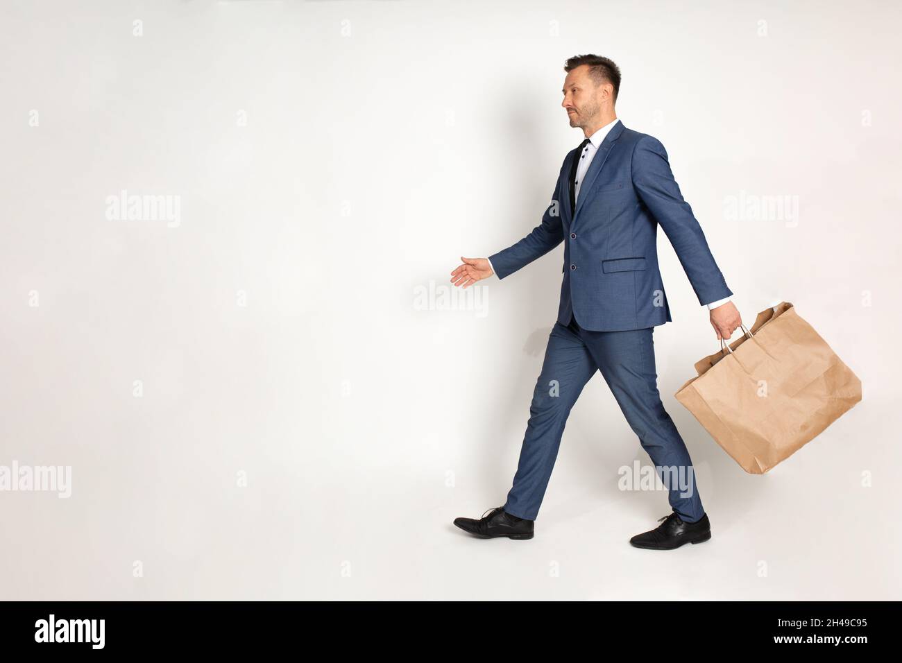 Homme d'affaires en costume marcher avec sac en papier d'artisanat dans la main, matériel de recyclage, achats, rabais et vente, modèle,Service de livraison.Prise de vue en studio Banque D'Images