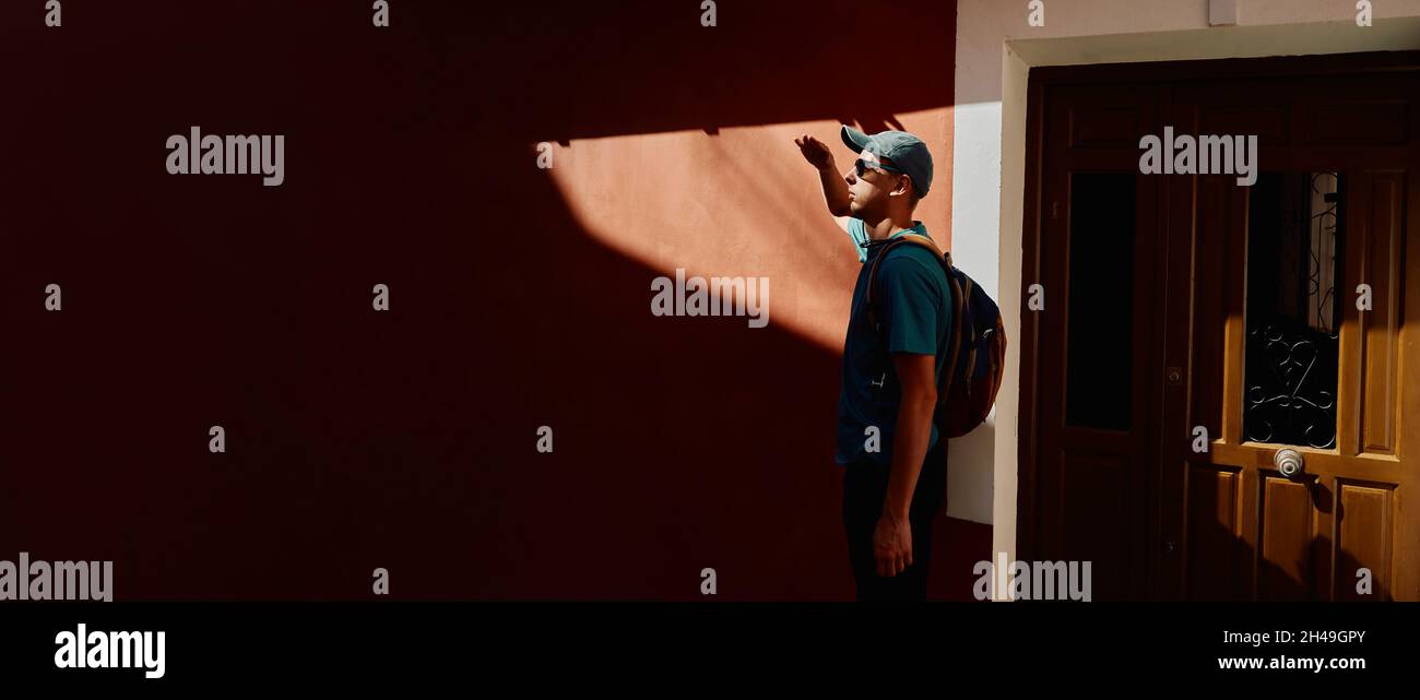 Homme voyageur debout près du mur urbain rouge avec la lumière du soleil dure et les ombres sombres. concept de voyageur Banque D'Images
