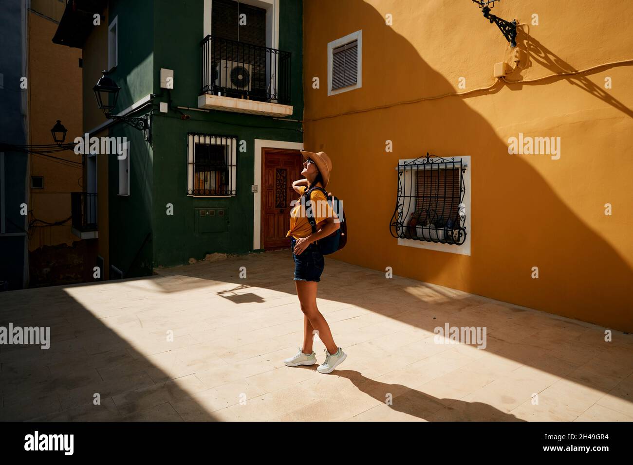 Femme voyageur avec sac à dos et chapeau de paille regardant les bâtiments colorés et les maisons Villajoyosa ville dans la journée ensoleillée Banque D'Images