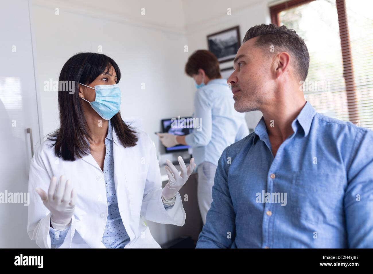 Dentiste biracial féminin portant un masque facial et parlant avec un patient masculin à la clinique dentaire moderne Banque D'Images