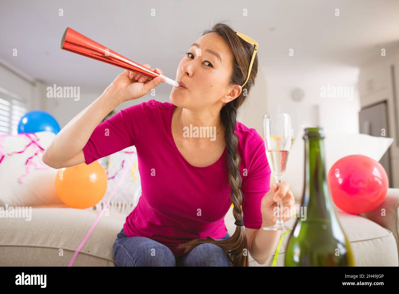 Bonne femme asiatique qui élève une trompette et une coupe de champagne pour passer un appel vidéo sur ordinateur portable le soir du nouvel an Banque D'Images