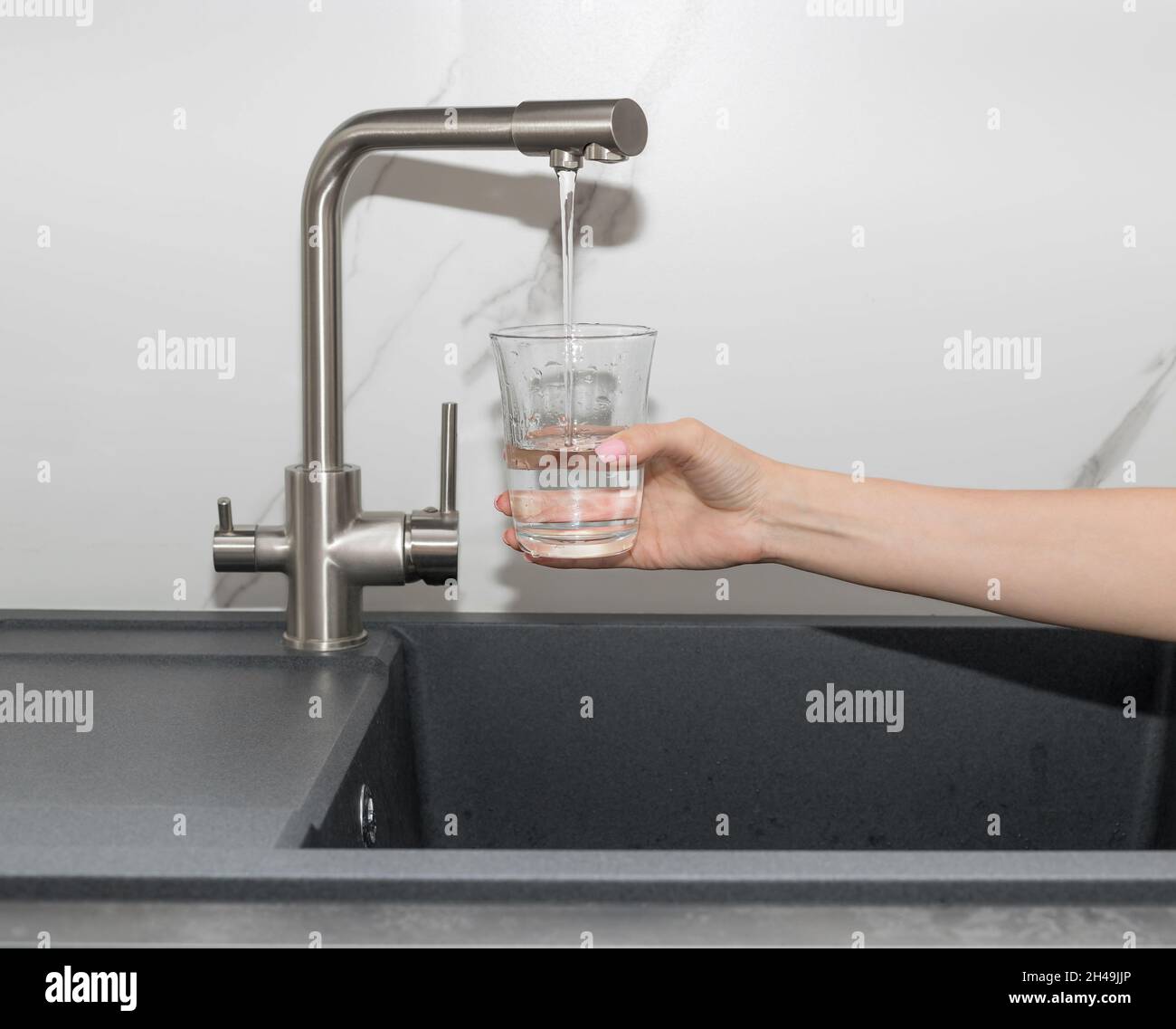 Femme versant de l'eau filtrée du robinet dans le verre de la cuisine Banque D'Images