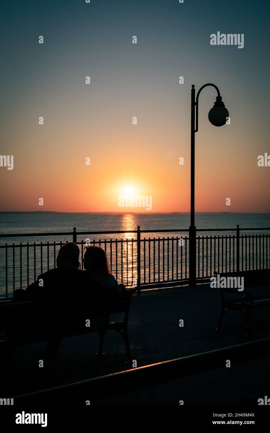 Miedzyzdroje, Pologne - 10 septembre 2021. Silhouettes d'un couple assis sur un banc sur une jetée, en admirant le coucher du soleil. Mer Baltique, Miedzyzdroje, Pologne. Banque D'Images