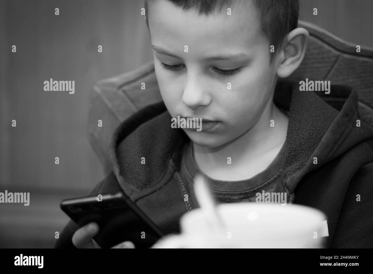 Bébé garçon de sept ans joue sur smartphone à la table, image en noir et blanc Banque D'Images