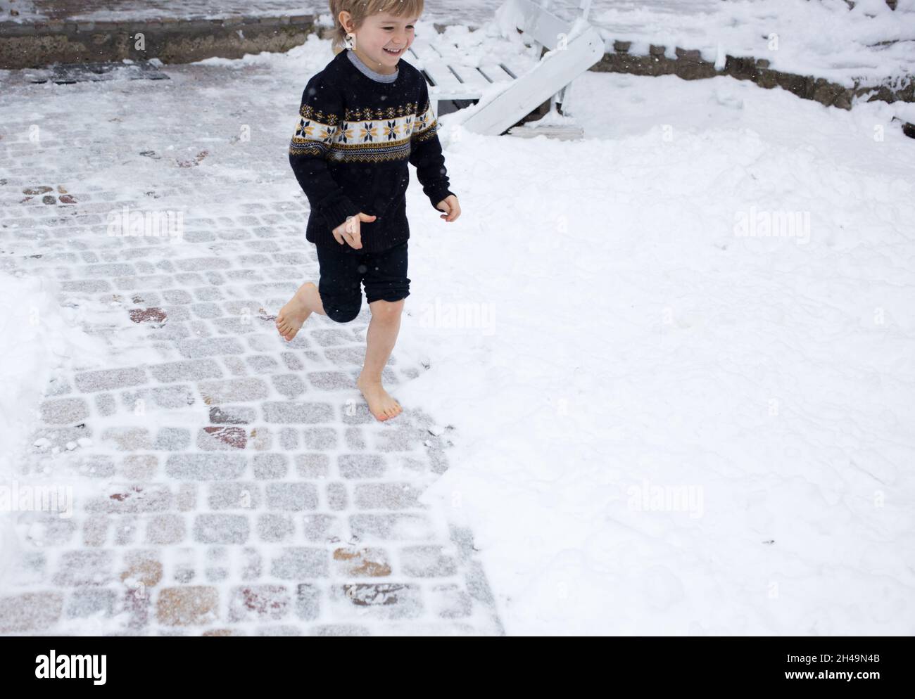 le garçon pieds nus de 4-5 ans court joyeusement dans la neige. concept de soins de santé, durcissement, chute de neige, temps froid. vacances actives d'hiver.Aime le Mo Banque D'Images