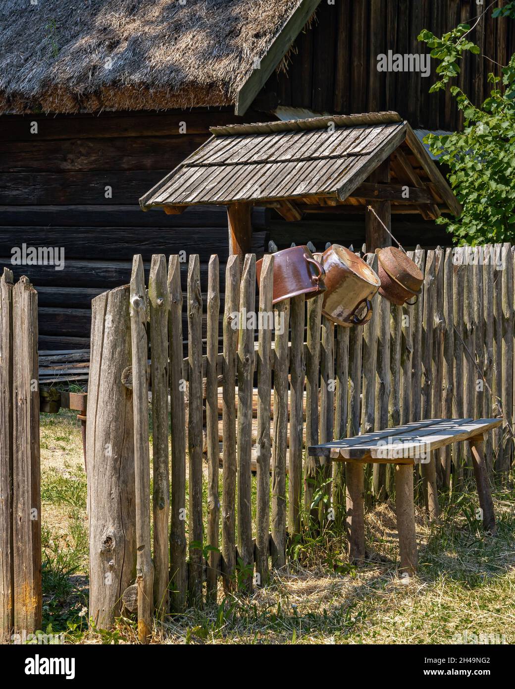 OPOLE, POLOGNE - 20 juin 2021: Pots d'argile suspendus sur une vieille clôture en bois, et un petit banc, devant un cottage traditionnel en bois. Banque D'Images