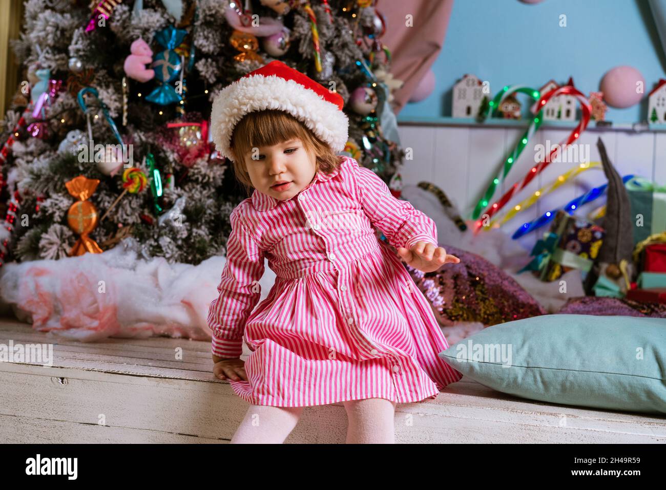 Petite fille sous l'arbre de noël en robe rose se trouve sur le plancher  fille portant le chapeau de père noël est en attente pour des cadeaux pour  noël et la nouvelle