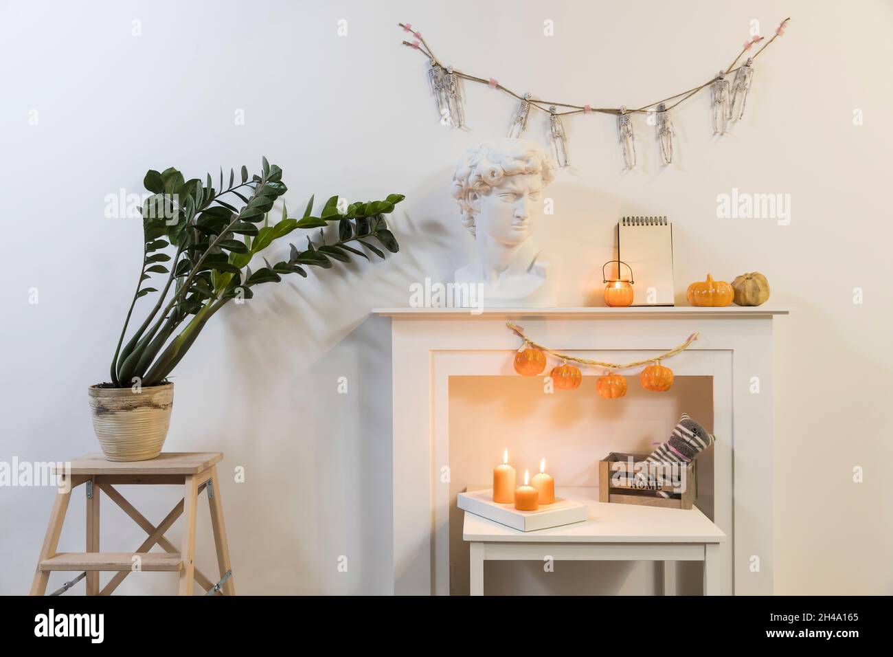 Tête en plâtre d'Apollo. Usine de Zamioculcas en pot d'argile sur tabouret.  Une guirlande de squelettes est suspendue au mur. Une guirlande de  citrouilles en plastique est suspendue au firemplacer Photo Stock -