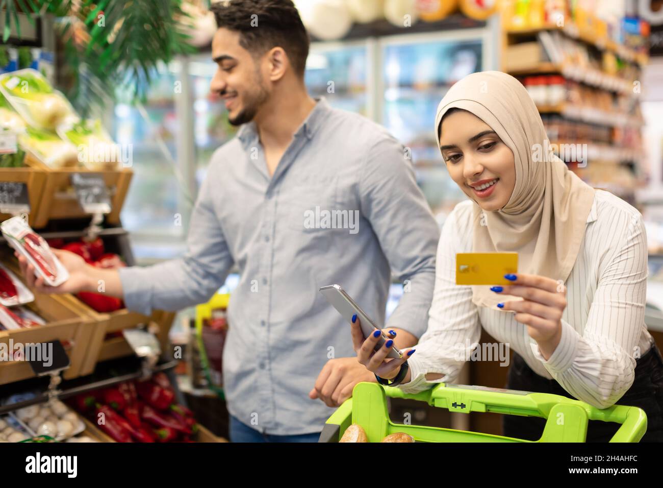 Couple islamique Acheter de la nourriture dans l'application mobile pour l'épicerie Shopping en utilisant le smartphone et la carte de crédit debout avec le chariot de magasin dans le magasin à l'intérieur.Groce Banque D'Images