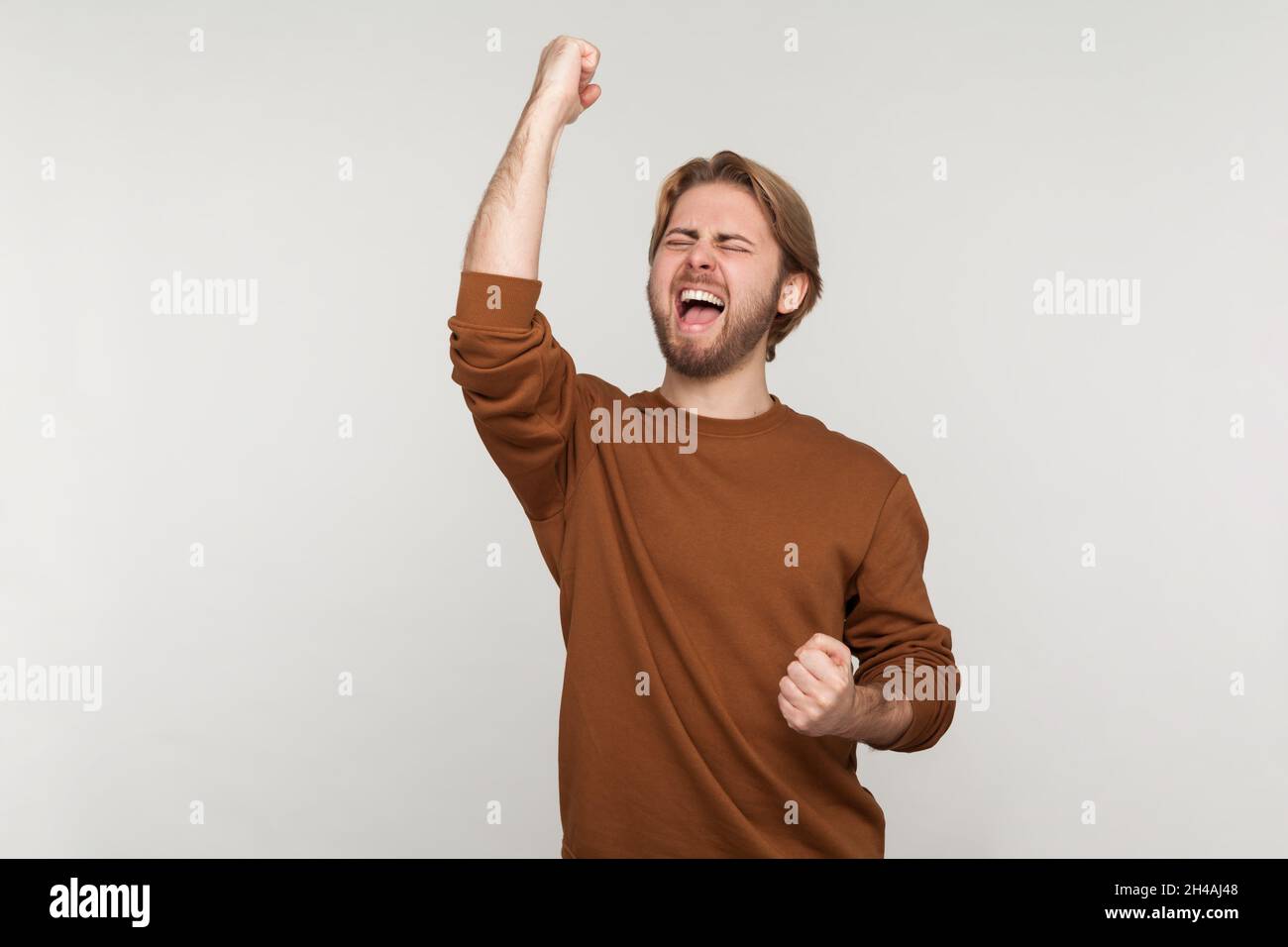 Portrait d'un homme excité avec un sweat-shirt à barbe, exprimant le geste gagnant avec des poings relevés et hurlant, célébrant la victoire.Prise de vue en studio isolée sur fond gris. Banque D'Images Portrait d'un homme excité avec un sweat-shirt à barbe, exprimant le geste gagnant avec des poings relevés et hurlant, célébrant la victoire.Prise de vue en studio isolée sur fond gris. Banque D'Images