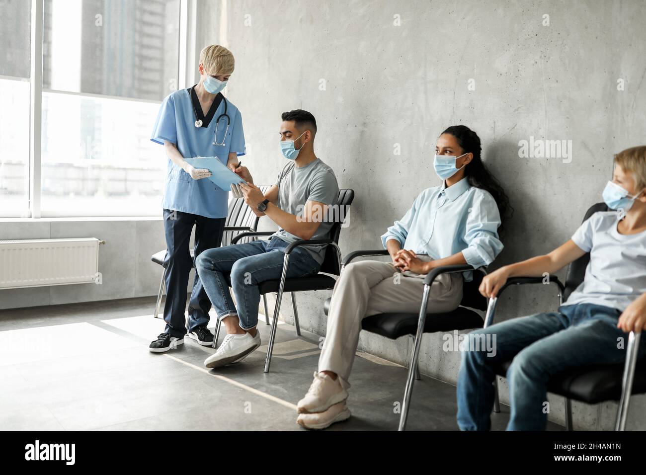 Jeune homme du Moyen-Orient, patient remplissant les papiers avant la vaccination, femme médecin aidant groupe multiracial d'adultes et d'âge scolaire, en attente de f Banque D'Images