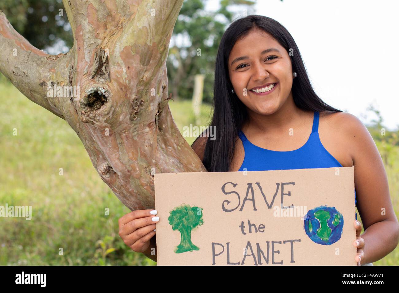 Une jeune fille adulte tient une affiche appelant à sauver la planète tout en embrassant un arbre.Portrait de la femme brune sur un fond naturel.ENREGISTREZ LE Banque D'Images