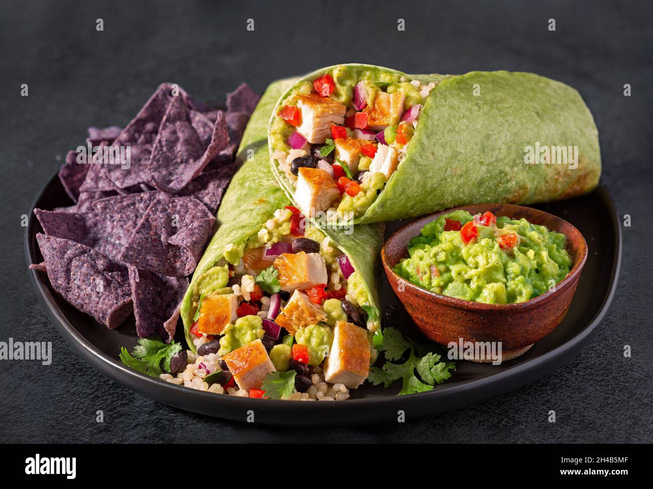 Burrito de poulet et de haricots noirs dans une enveloppe d'épinards avec des chips de tortilla de maïs bleu et des guacomole Banque D'Images