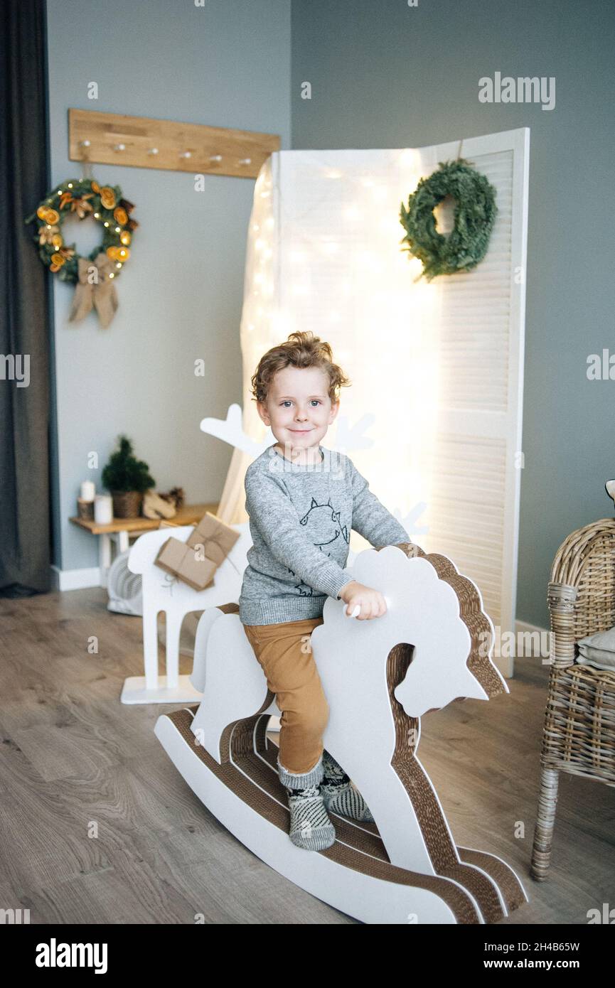 Petit garçon assis sur un cheval en bois dans la chambre décorée de noël. Banque D'Images