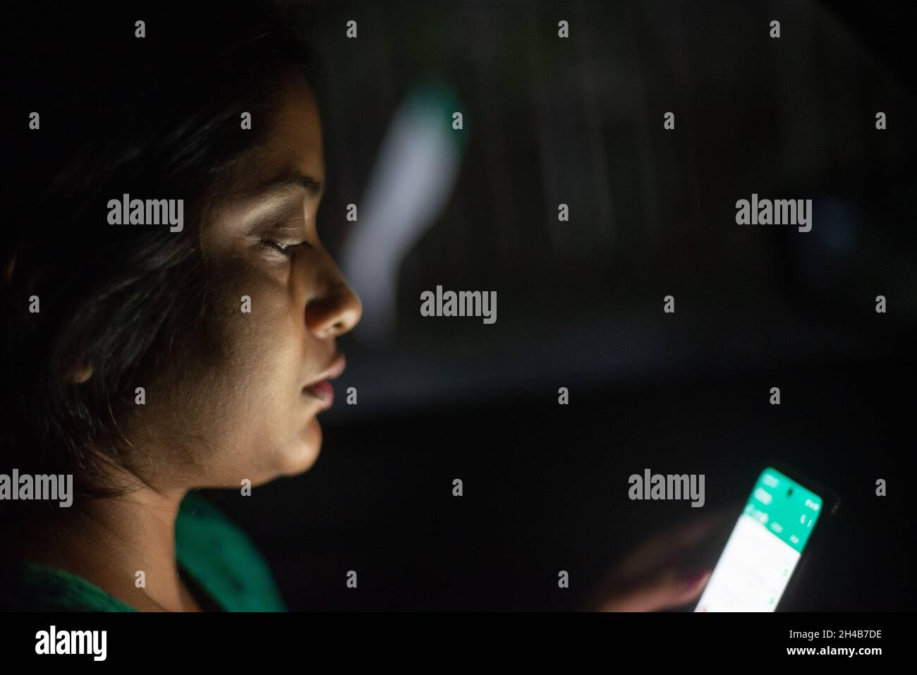 Femme indienne regardant son téléphone portable assis à l'intérieur d'une voiture dans l'obscurité Banque D'Images
