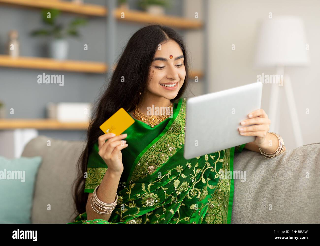 Jolie femme indienne dans l'ethnie sari robe utilisant la tablette numérique et carte de crédit pour le shopping en ligne à la maison.Jolie femelle de l'est en tenue nationale buyi Banque D'Images