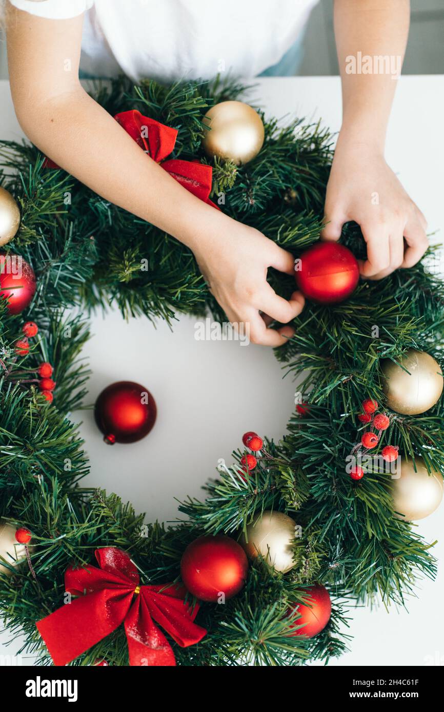 Vue de dessus des mains des enfants décorant la couronne de Noël avec des jouets et des noeuds de Noël rouges.Avent pour enfants, bricolage. Banque D'Images