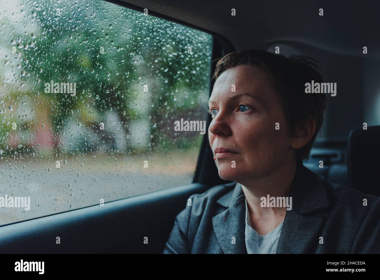 Femme d'affaires inquiète attendant dans la voiture et regardant par la fenêtre pendant la pluie, mise au point sélective Banque D'Images