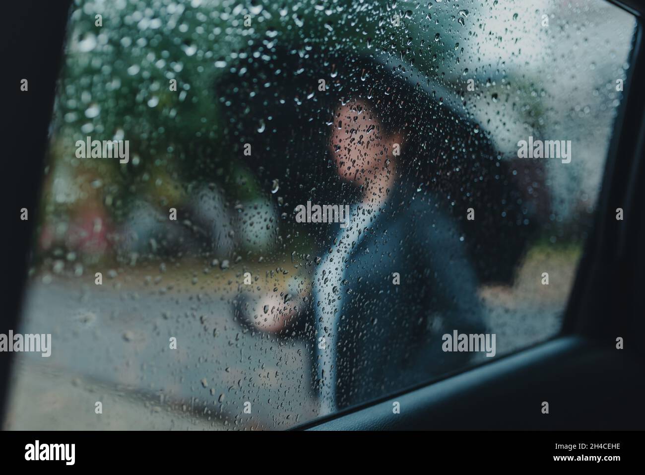 Femme d'affaires avec parapluie attendant dans la pluie à l'extérieur de la voiture, foyer sélectif Banque D'Images