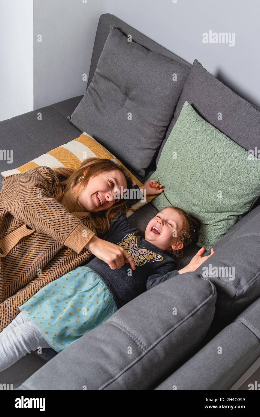 Maman tille sa fille fermement tout en étant couché sur le canapé confortable de la maison.Rire de la famille en s'amusant ensemble Banque D'Images