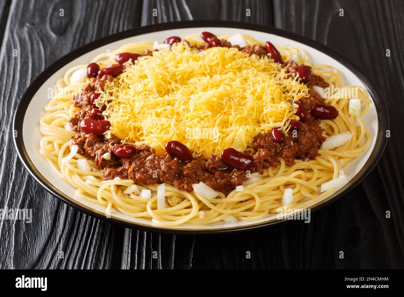 Délicieux piment de Cincinnati avec spaghetti, cheddar, oignons frais et haricots dans une assiette sur la table. Horizontal Banque D'Images