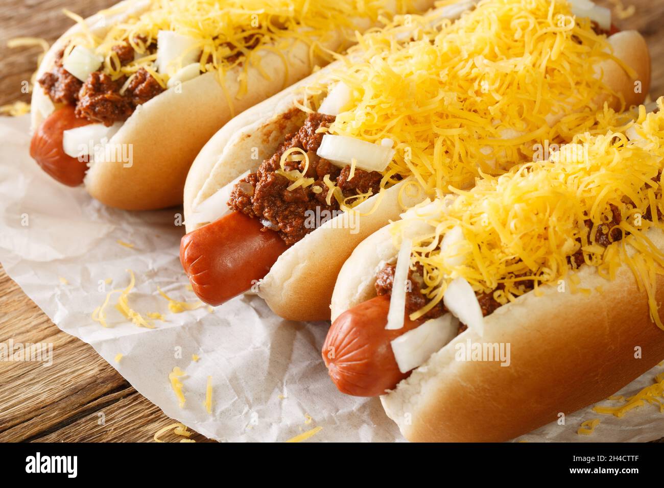 Chien chaud de bœuf dans un petit pain recouvert de Chili de Cincinnati, dés d'oignons et une masse de fromage cheddar râpé dans le papier sur la table.Horizonta Banque D'Images