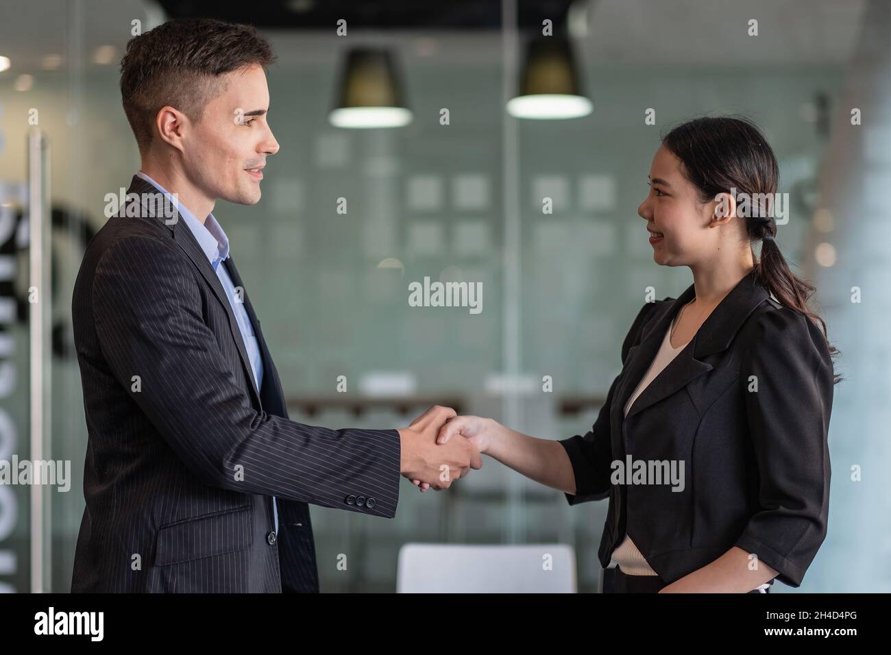 Heureux partenaires d'affaires positifs finissant la réunion.Homme d'affaires et femme debout au bureau, se serrer les mains, sourire, parler.Concept de poignée de main Banque D'Images