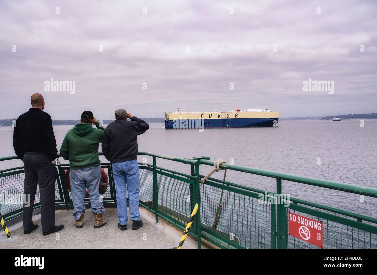 Seattle, WA, États-Unis - 14 juin 20014 : trois passagers de ferry regardent un porte-mer Eukor se déplacer à travers Puget Sound alors qu'ils se rendent dans le centre-ville de S. Banque D'Images
