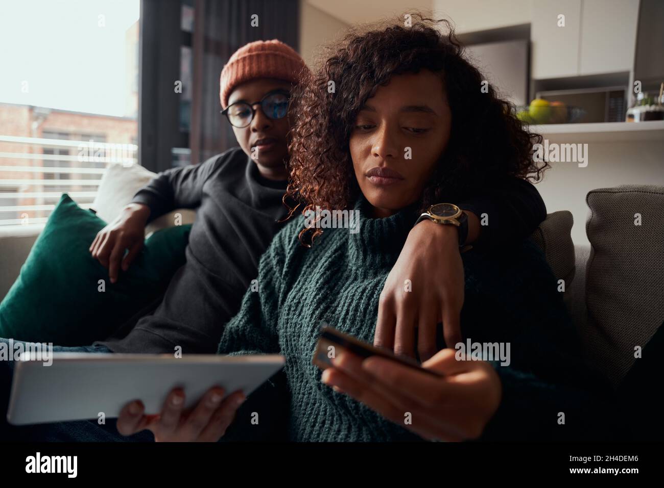 Couple adulte, multi-ethnique, préoccupé par le paiement en ligne sur tablette canapé dans l'appartement moderne Banque D'Images