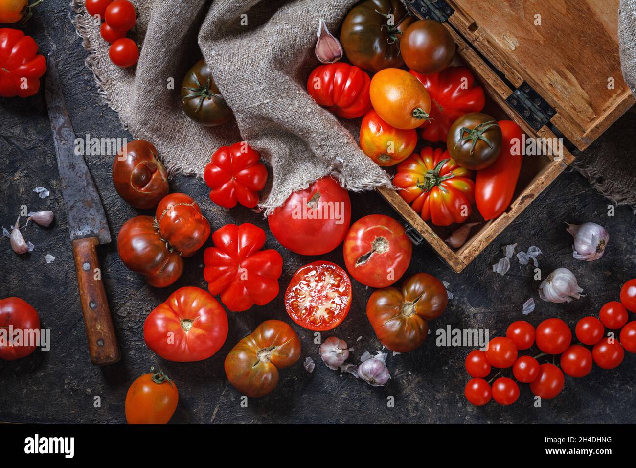 Cuisine encore vie avec des objets rétro, vue de dessus - tomates multicolores de différentes tailles et types, ail, couteau, boîte, toile.Le concept de cuisinier Banque D'Images
