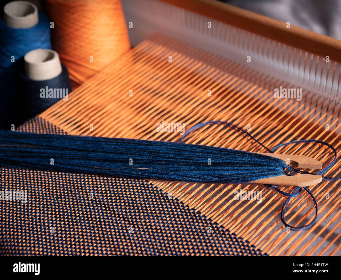 Création du textile bleu et orange à l'aide d'un métier à tisser.Métier à tisser en bois, navette et cônes avec fil.Vêtements fabriqués avec une main Banque D'Images