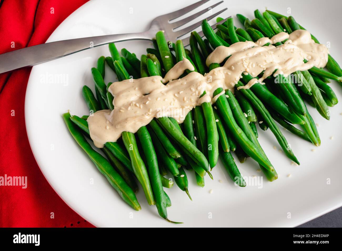 Haricots verts avec une sauce Dijon-Tahini et graines de sésame : un plateau de haricots avec sauce et graines de sésame Banque D'Images