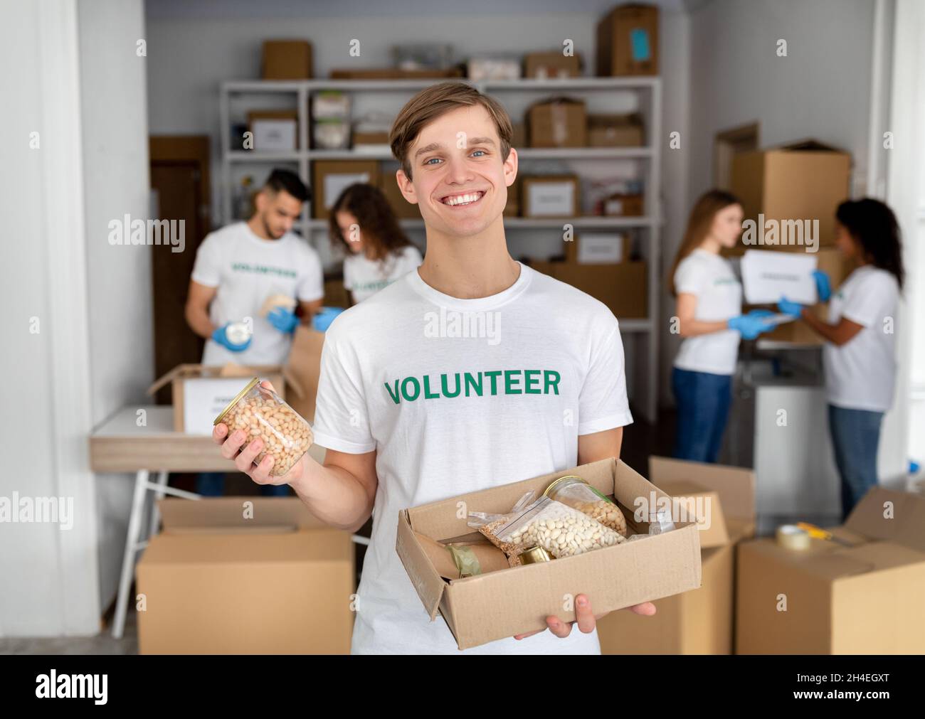 Aide humanitaire.Jeune homme de la tenue de bénévoles peut dans la main et la boîte avec des grains, travaillant au centre de charité Banque D'Images