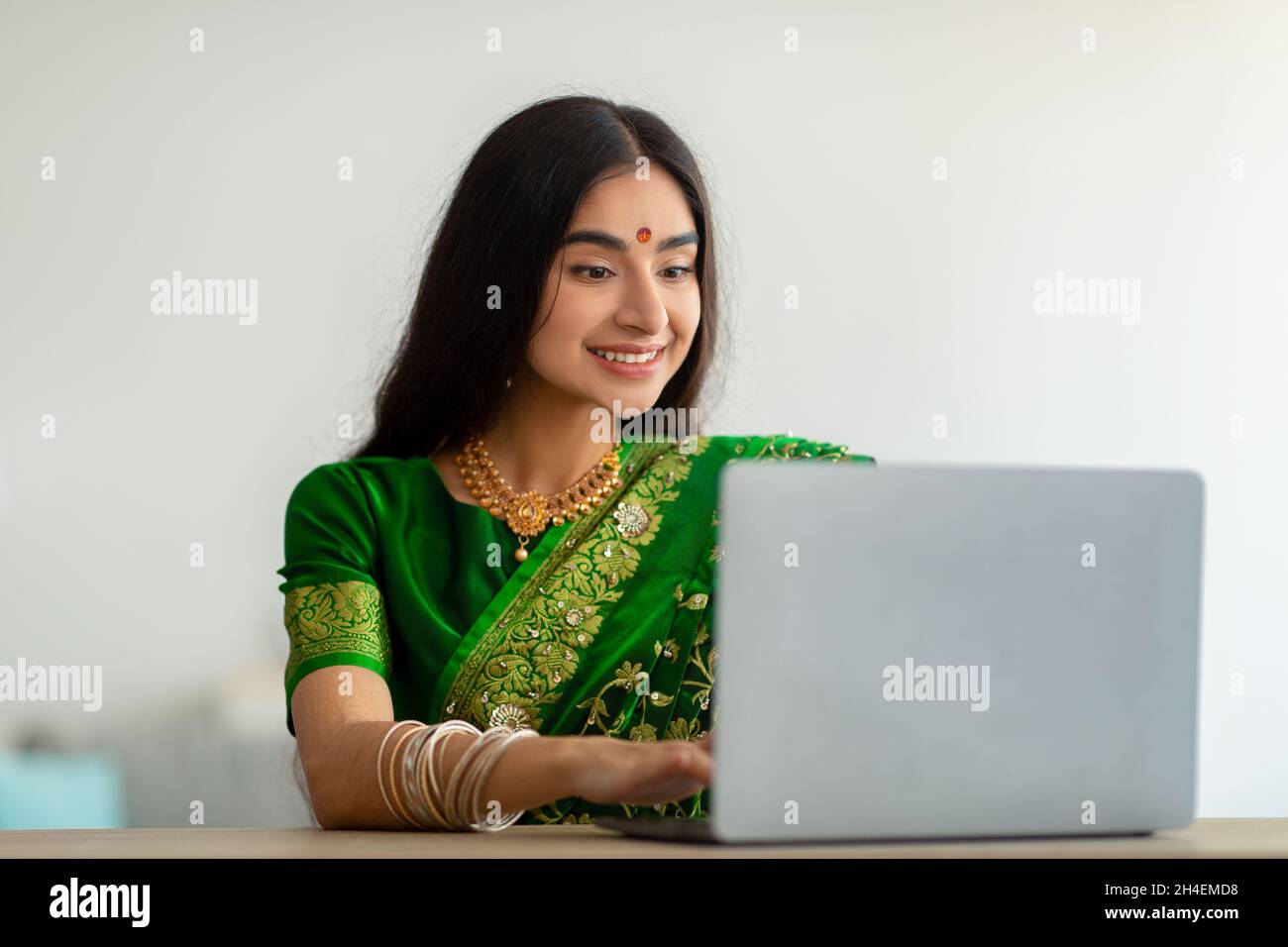 Femme indienne millénaire en robe sari élégante étudiant ou travaillant en ligne, en utilisant un ordinateur portable à la maison Banque D'Images